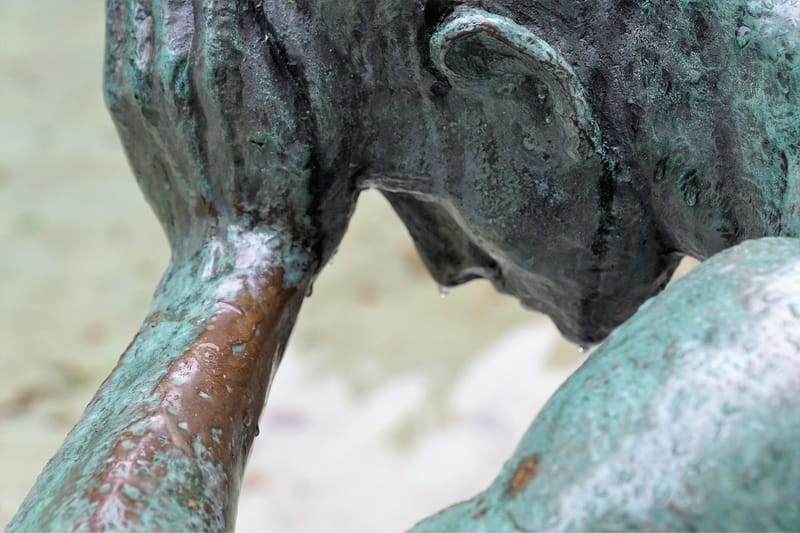 Statue en bronze d'une personne la tête appuyée sur le bras, l'air abattu